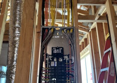 Electrical panel with multiple colored wires in a wooden frame of a building under construction. A red ladder stands nearby.
